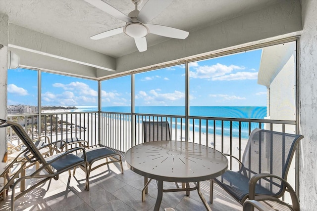 sunroom / solarium with a water view, ceiling fan, and a view of the beach