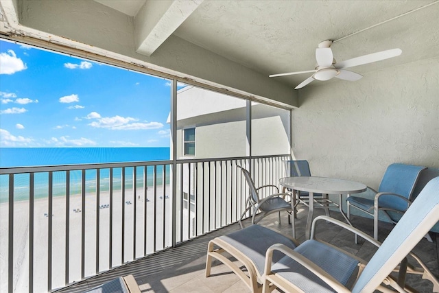 balcony featuring a view of the beach, ceiling fan, and a water view