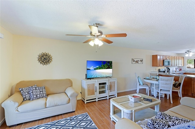 living room featuring ceiling fan, a textured ceiling, and light hardwood / wood-style floors