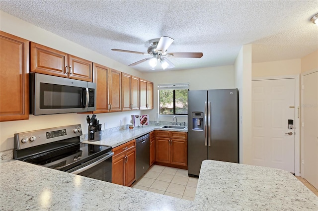 kitchen featuring appliances with stainless steel finishes, sink, light tile patterned floors, light stone countertops, and a textured ceiling