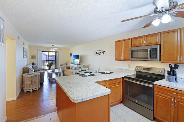 kitchen with ceiling fan, stainless steel appliances, light hardwood / wood-style floors, a textured ceiling, and kitchen peninsula