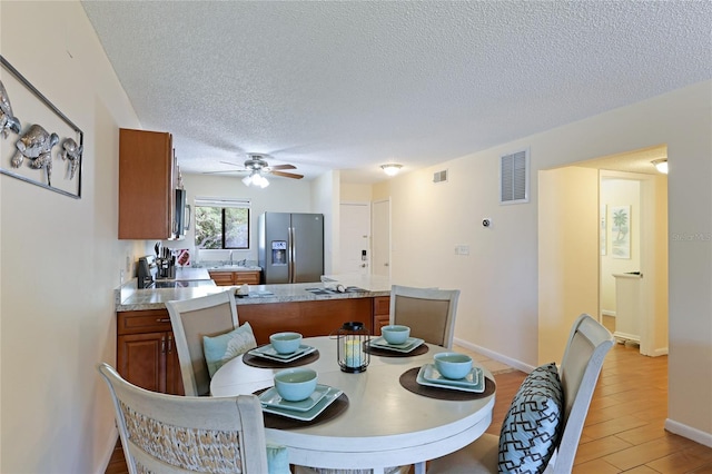 dining area featuring sink, light hardwood / wood-style floors, a textured ceiling, and ceiling fan