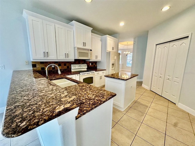 kitchen with white appliances, kitchen peninsula, white cabinets, and a kitchen island