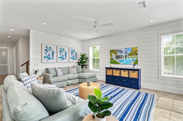 living room featuring light hardwood / wood-style floors, ceiling fan, and wooden walls