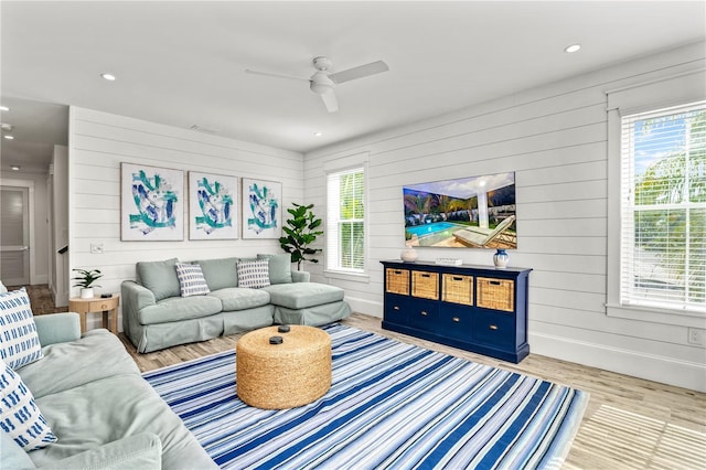 living room featuring ceiling fan, wooden walls, and light wood-type flooring