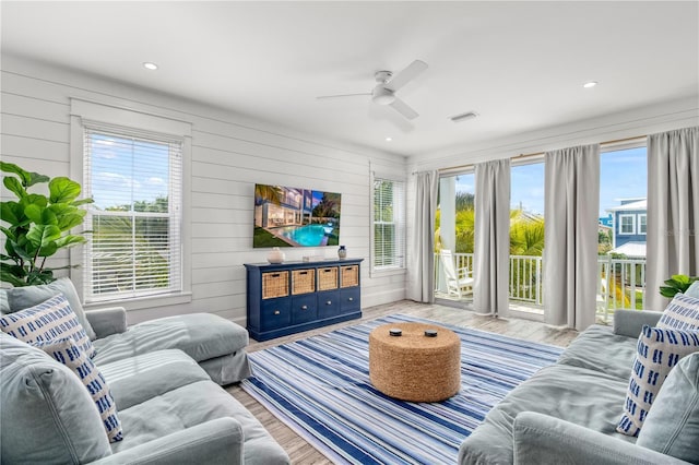 living room with ceiling fan, light wood-type flooring, and wood walls