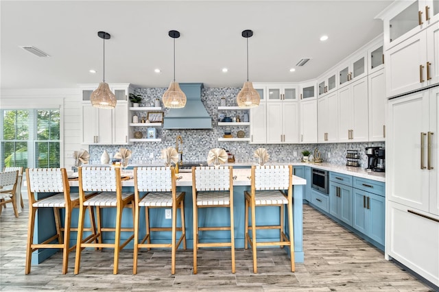 kitchen with pendant lighting, a kitchen island with sink, custom range hood, white cabinets, and blue cabinets