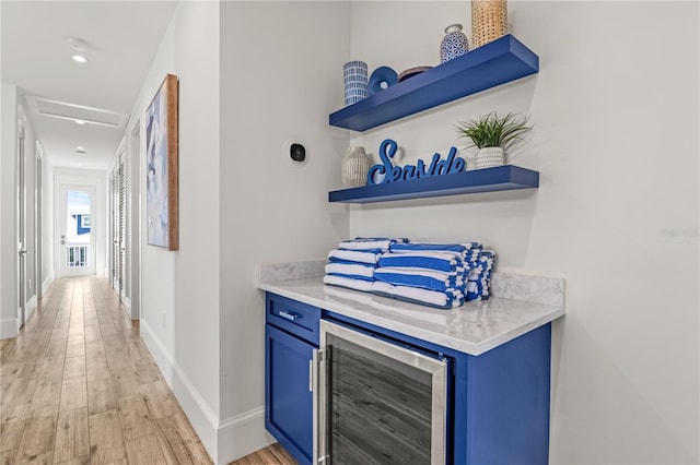 bar with light wood-type flooring, wine cooler, and blue cabinetry