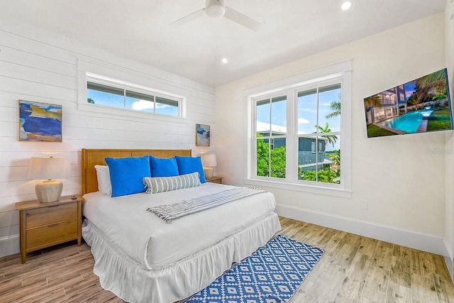 bedroom featuring ceiling fan, light hardwood / wood-style floors, and wooden walls