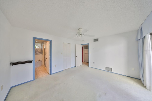 unfurnished bedroom featuring ceiling fan, connected bathroom, a textured ceiling, light carpet, and a closet