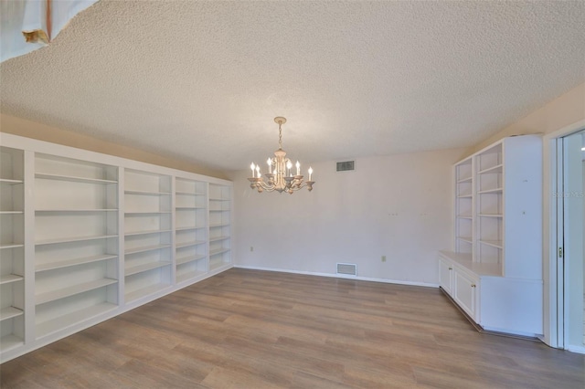 unfurnished dining area with built in shelves, light hardwood / wood-style flooring, a textured ceiling, and a notable chandelier