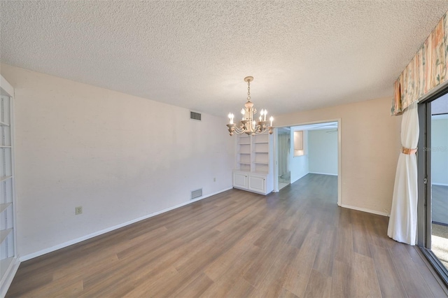 unfurnished dining area featuring dark wood-type flooring, built in features, a chandelier, and a textured ceiling