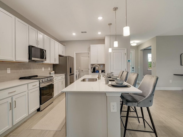 kitchen with sink, a breakfast bar area, appliances with stainless steel finishes, a kitchen island with sink, and white cabinetry