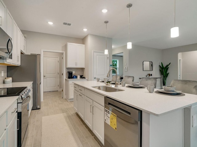 kitchen featuring appliances with stainless steel finishes, white cabinetry, sink, hanging light fixtures, and a kitchen island with sink