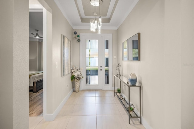 tiled foyer featuring a chandelier, ornamental molding, and a raised ceiling