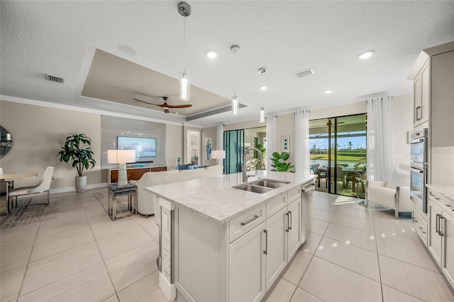 kitchen with decorative light fixtures, white cabinetry, an island with sink, sink, and a tray ceiling