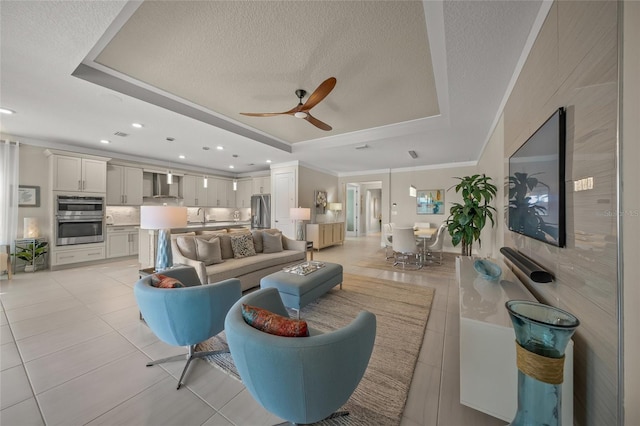 living room featuring light tile patterned flooring, a textured ceiling, ornamental molding, a tray ceiling, and ceiling fan