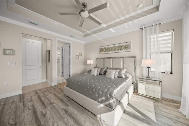 bedroom featuring ceiling fan, a raised ceiling, and light wood-type flooring