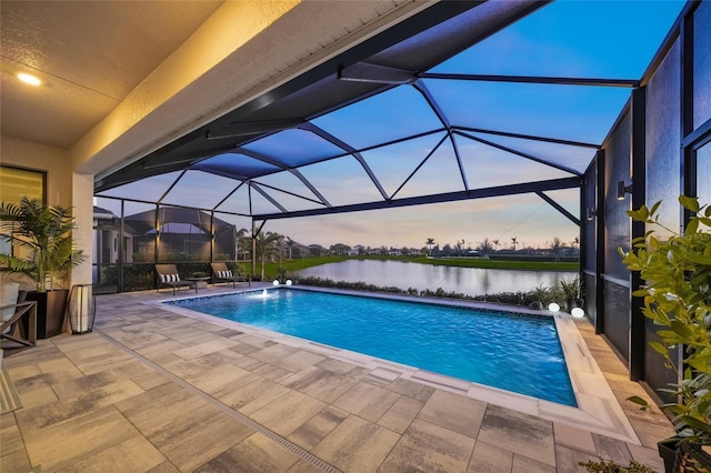 pool at dusk featuring a water view, a patio area, pool water feature, and a lanai