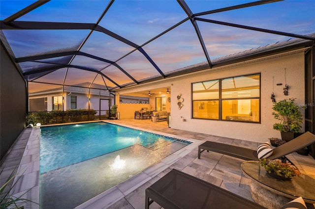 pool at dusk featuring ceiling fan, an outdoor living space, a patio area, and glass enclosure