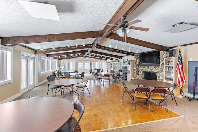 dining space with ceiling fan, a textured ceiling, lofted ceiling with beams, and a fireplace