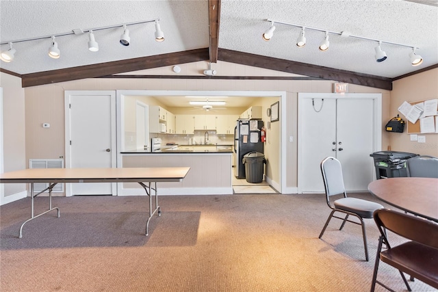 kitchen with white cabinets, stainless steel fridge, lofted ceiling with beams, light colored carpet, and stove