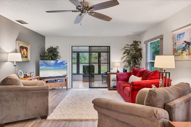 living room featuring ceiling fan, plenty of natural light, a textured ceiling, and light hardwood / wood-style flooring