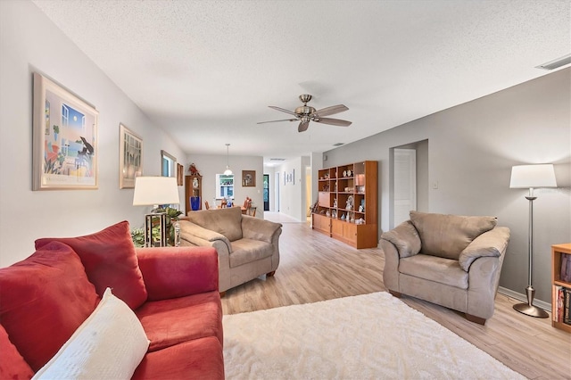 living room with ceiling fan, light hardwood / wood-style floors, and a textured ceiling