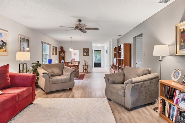 living room featuring ceiling fan, a textured ceiling, and light wood-type flooring