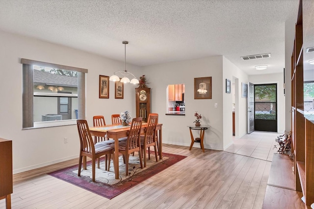 dining area with an inviting chandelier, a textured ceiling, and light wood-type flooring