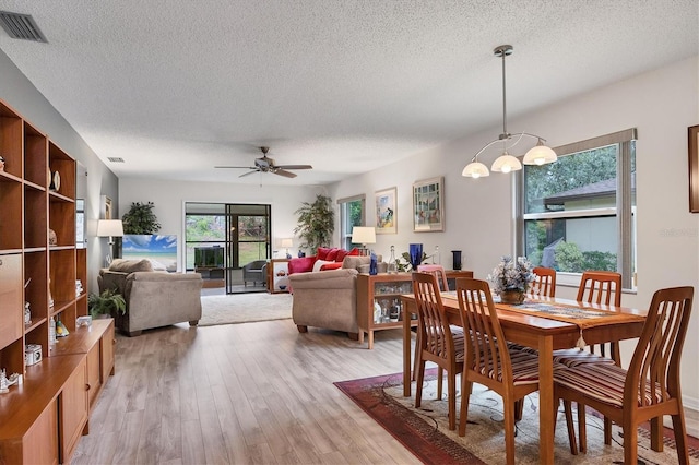 dining space with ceiling fan with notable chandelier, a textured ceiling, and light wood-type flooring