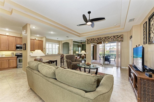 tiled living room featuring ceiling fan and a tray ceiling