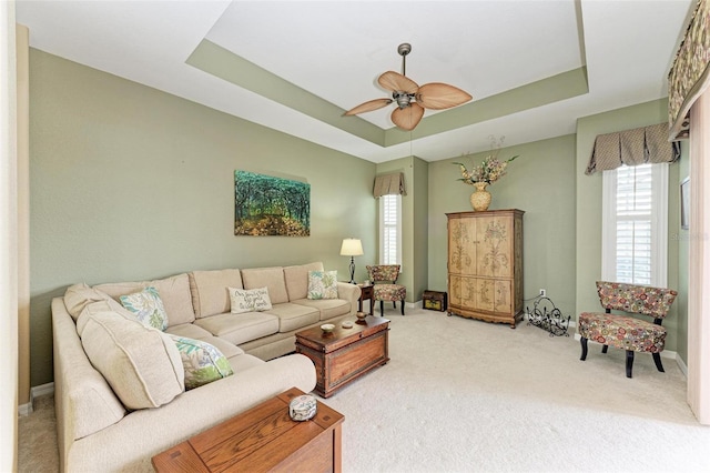 carpeted living room with ceiling fan and a tray ceiling