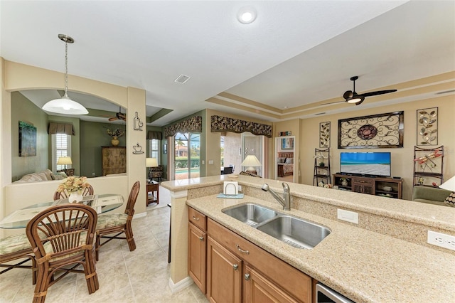 kitchen with ceiling fan, hanging light fixtures, sink, a tray ceiling, and light stone counters