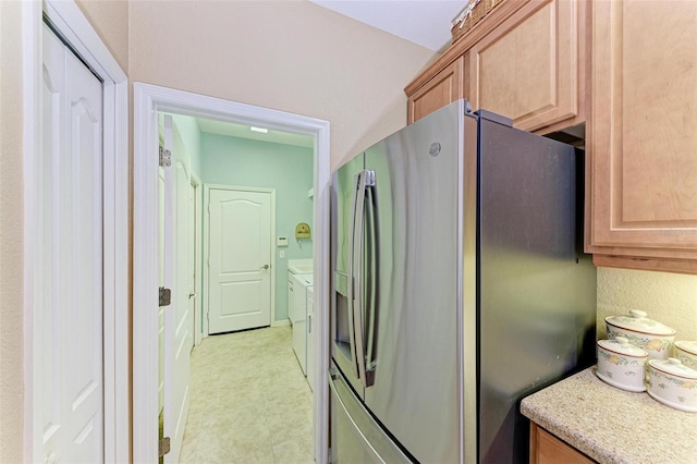 kitchen with separate washer and dryer, stainless steel fridge with ice dispenser, and light stone countertops