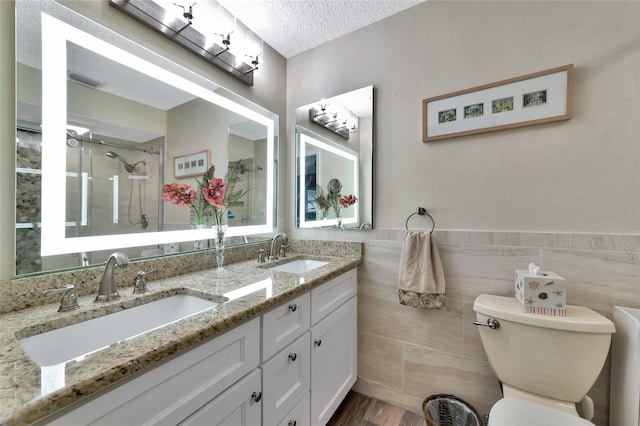 bathroom featuring a textured ceiling, an enclosed shower, vanity, tile walls, and toilet