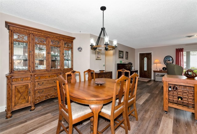 dining space featuring dark wood-type flooring, a textured ceiling, and an inviting chandelier