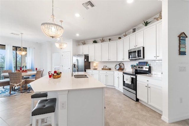 kitchen featuring an island with sink, white cabinetry, hanging light fixtures, and stainless steel appliances