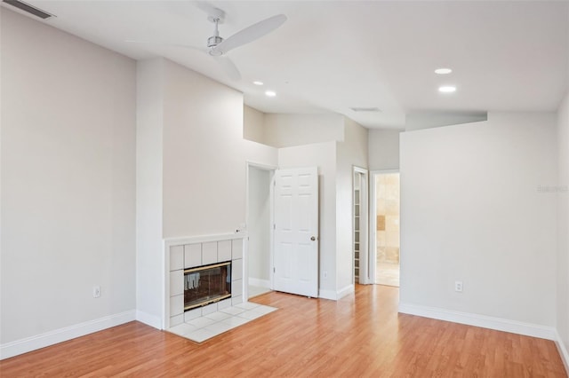 unfurnished living room with a tile fireplace, ceiling fan, and light wood-type flooring