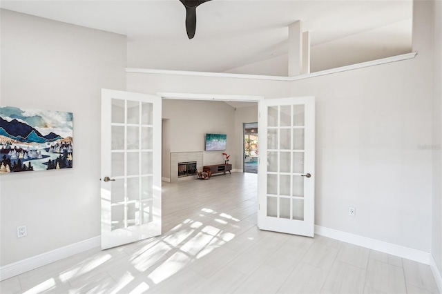 unfurnished room featuring a tiled fireplace, lofted ceiling, and french doors