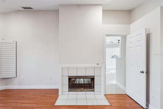 unfurnished living room featuring baseboards, visible vents, wood finished floors, and a tile fireplace