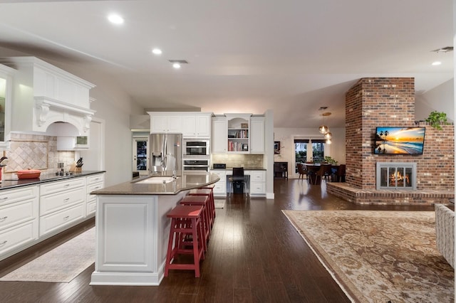 kitchen featuring a kitchen island with sink, decorative backsplash, white cabinetry, and appliances with stainless steel finishes