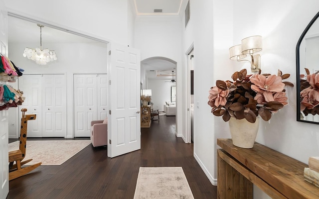 corridor featuring dark wood-type flooring, a towering ceiling, and a notable chandelier