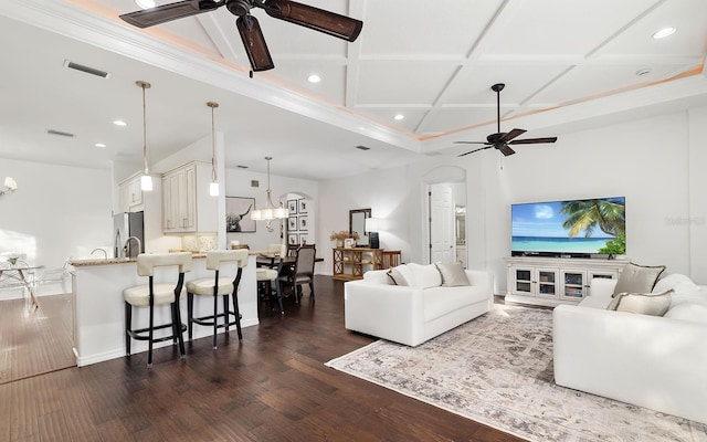 living room featuring dark wood-type flooring, ceiling fan with notable chandelier, and coffered ceiling