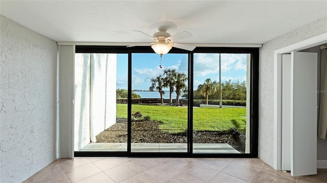 doorway to outside with expansive windows, ceiling fan, and light tile patterned floors