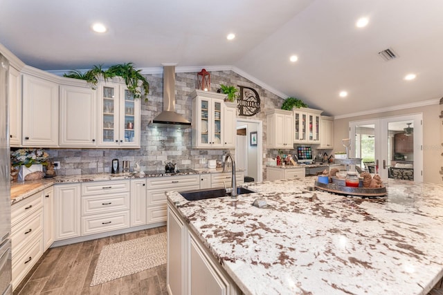 kitchen featuring light stone countertops, tasteful backsplash, sink, vaulted ceiling, and wall chimney exhaust hood