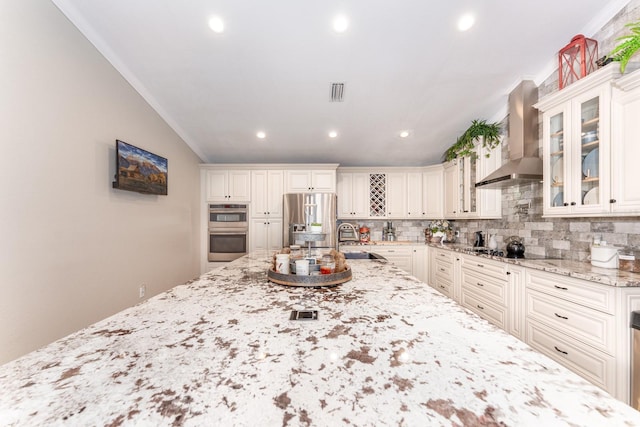 kitchen featuring light stone countertops, wall chimney range hood, stainless steel appliances, tasteful backsplash, and sink