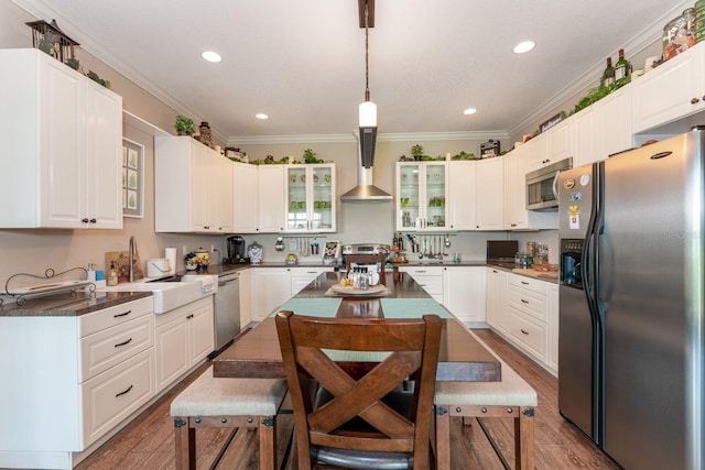 kitchen featuring wall chimney range hood, stainless steel appliances, white cabinetry, and hanging light fixtures