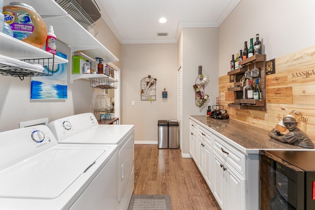 laundry area featuring crown molding, wine cooler, light wood-type flooring, washer and dryer, and bar area