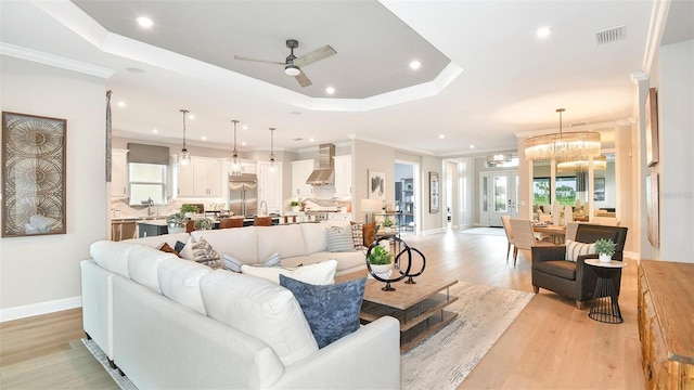 living room featuring crown molding, ceiling fan with notable chandelier, a tray ceiling, and light hardwood / wood-style floors